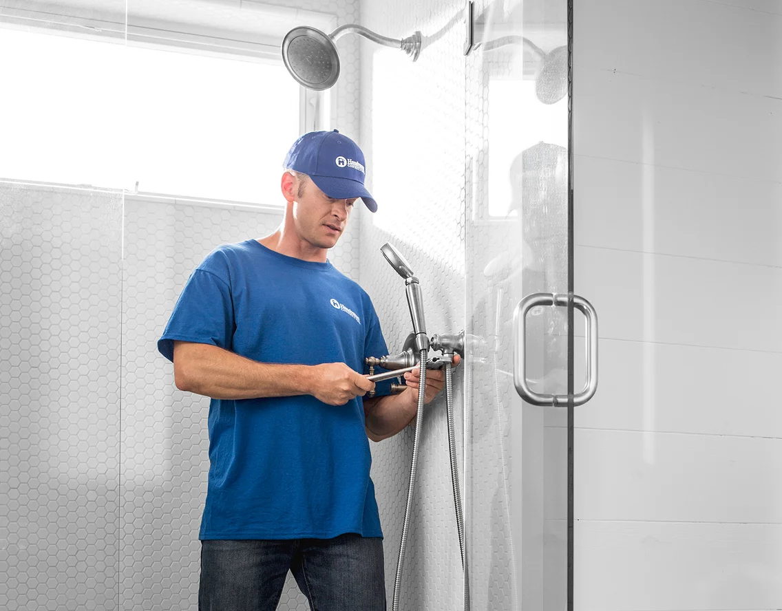 Professional plumber installing shower fixtures inside a glass-enclosed tiled shower.